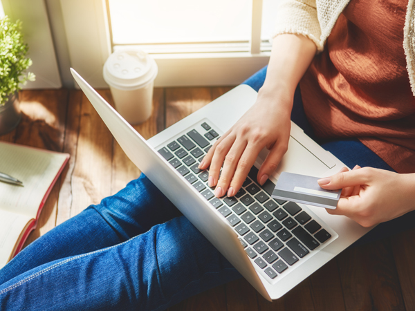 Person sitting on the floor, holding a credit card, and using a laptop