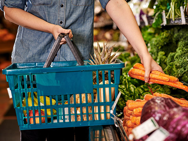 a woman adds fruits and vegetables into her shopping basket