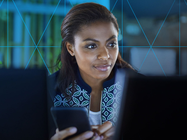 Professional woman using a computer and smartphone, with blue digital grid overlay.