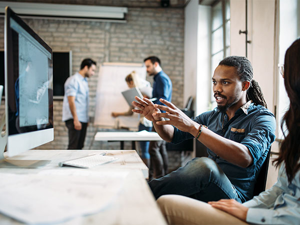 main pointing at a computer screen explaining something to a coworker