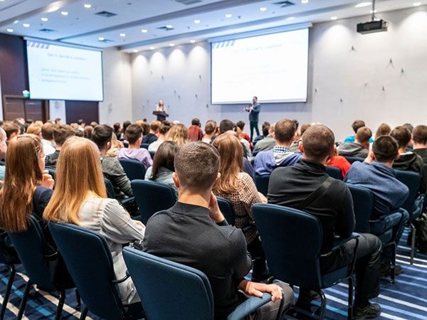 People sitting in a large conference room listening to a presenter in the front of the room