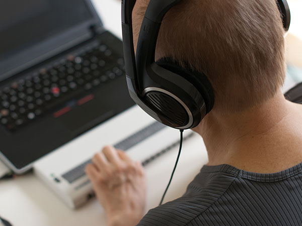 photo looking over the sholder of a man wearing headphones while working on an accessibly modified laptop
