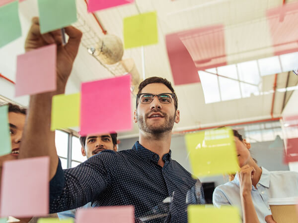 Man smiling and meeting at office use post it notes to share idea and planning project. Group of employee brainstorming idea on glass