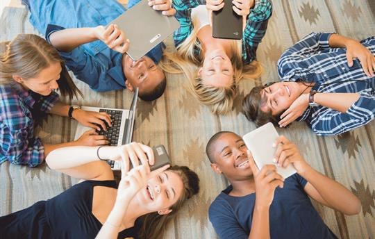 Teens on phones, tablets, and a laptop displaying a multichannel approach.