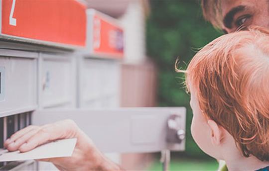 a man and toddler looking into their mailbox while retrieving a piece of mail